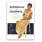 Book cover for 'Joernal met Journal with Lynette Beer' featuring a photo of Lynette Beer sitting on a white stool, wearing a vibrant multicolor patterned dress. The cover has a white background with dark navy and yellow text.